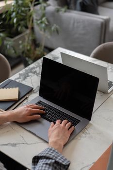 Person typing on a black laptop at a marble desk with greenery in the background.