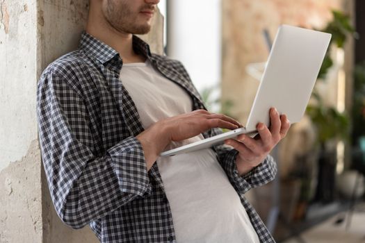 Casual young man in plaid shirt using laptop indoors. Modern lifestyle and technology.