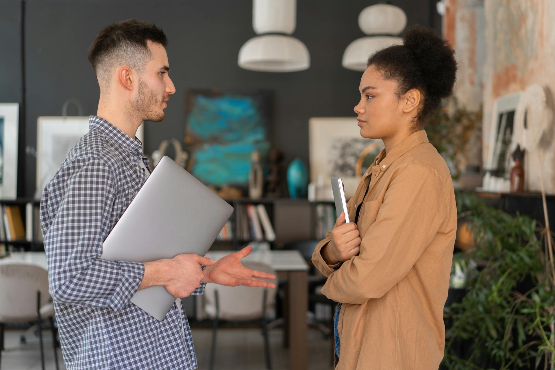 Two office workers engaged in a conversation, holding devices, in a modern office setting.