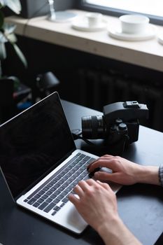 An overhead view of hands typing on a laptop next to a camera on a table.