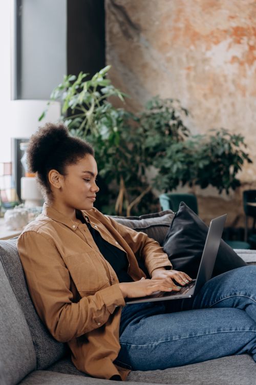 Free African American woman relaxed on couch using laptop, working in cozy indoor setting. Stock Photo