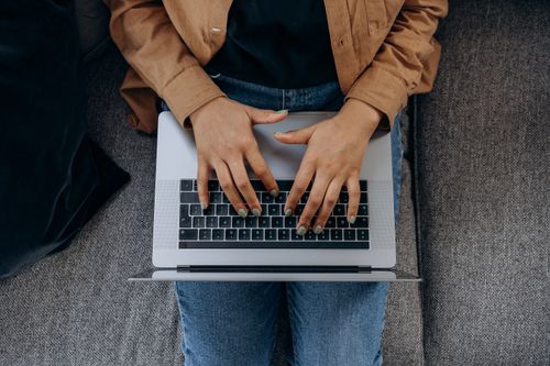 Free A woman types on her laptop while sitting on a sofa, viewed from above. Stock Photo
