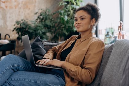 A confident woman working remotely on a laptop, sitting comfortably at home — photo by Mikhail Nilov on Pexels