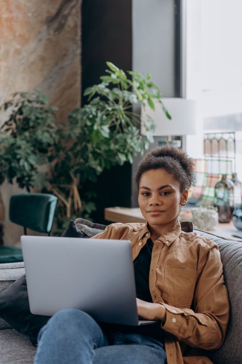 Free Confident African American woman working on a laptop in a comfortable indoor setting with modern decor. Stock Photo