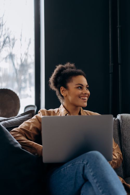 Free African American woman smiling while working on laptop indoors. Stock Photo