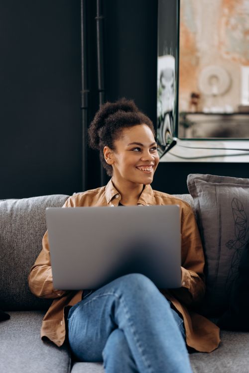 Free A cheerful woman sits with a laptop indoors, embodying a relaxed and modern digital lifestyle. Stock Photo