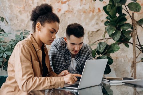 Free Two young adults collaborate on a project using a laptop in a modern workspace. Stock Photo