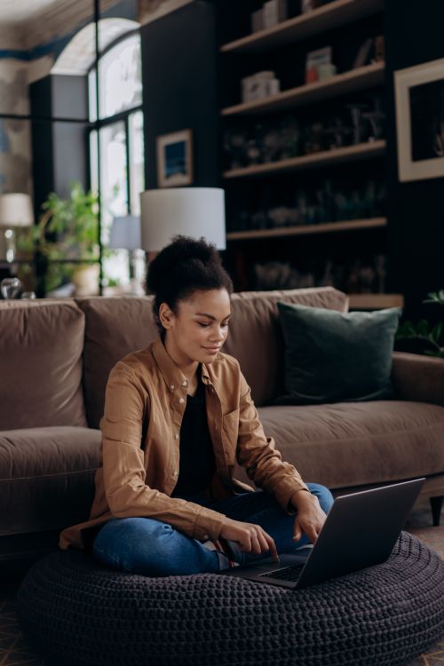 Free African American woman using laptop for remote work at home on a cozy sofa setup. Stock Photo