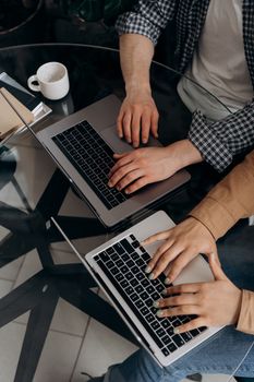Two people using laptops at a glass table, top view, showcasing teamwork.