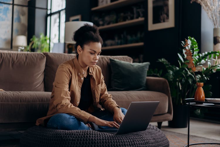 Woman Sitting On Black Knitted Floor Cushion While Using Laptop