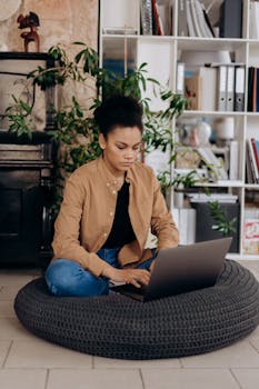 African American woman working on a laptop at home, sitting comfortably on a cushion.