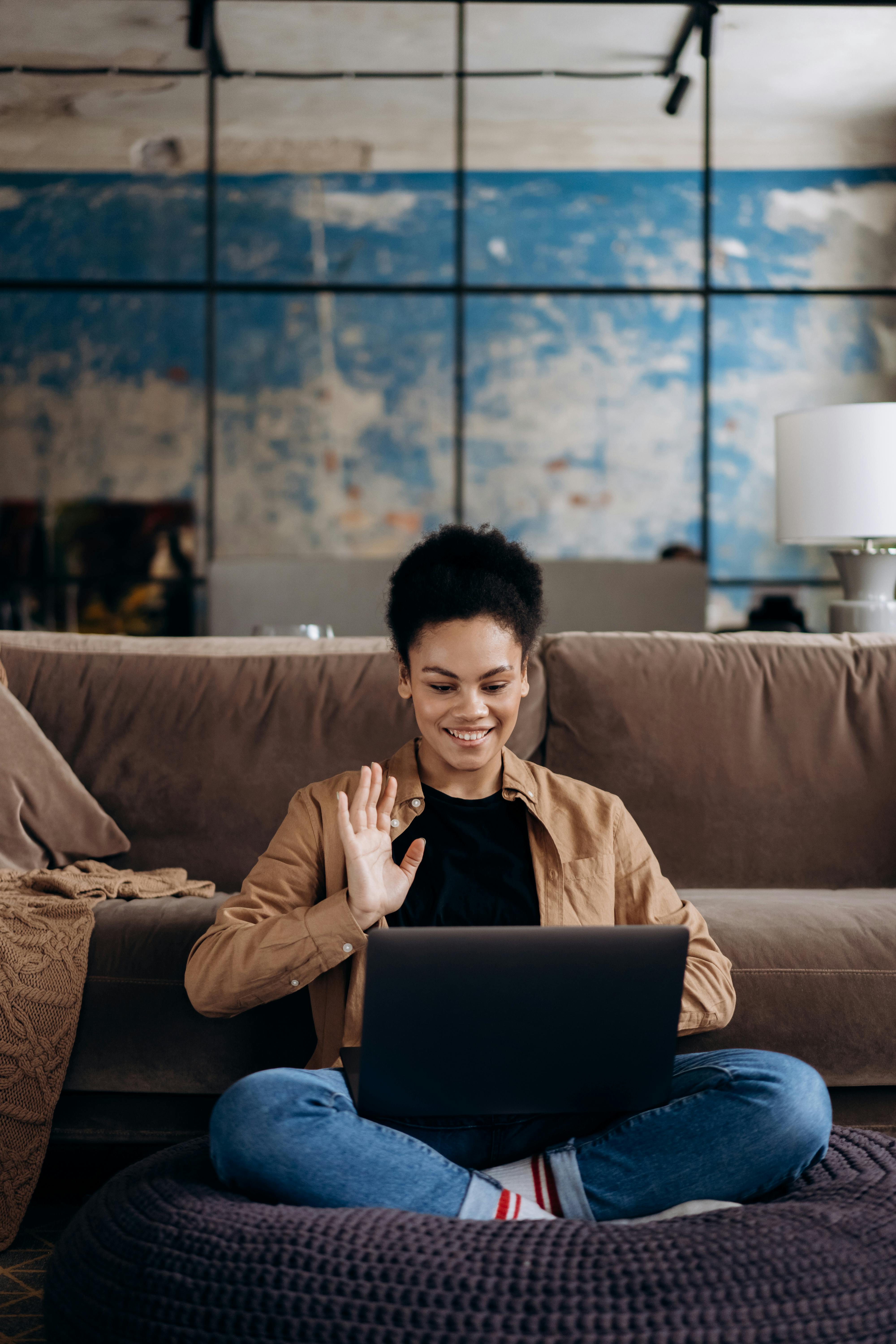 man in brown dress shirt and blue denim jeans sitting on brown couch using black laptop