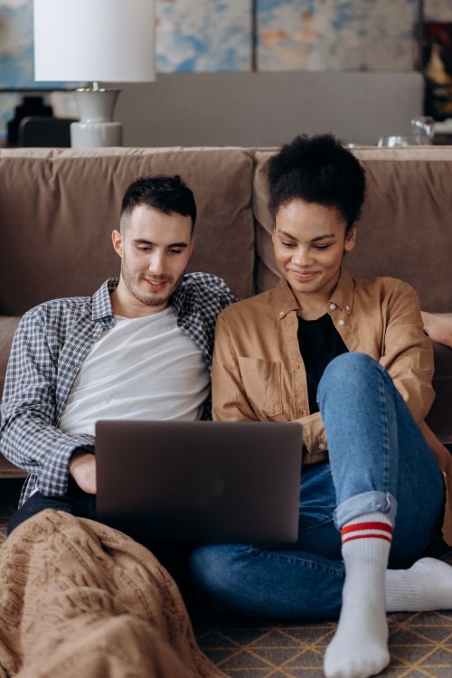 Free A young couple sitting on a couch, studying together using a laptop in a cozy living room. Stock Photo