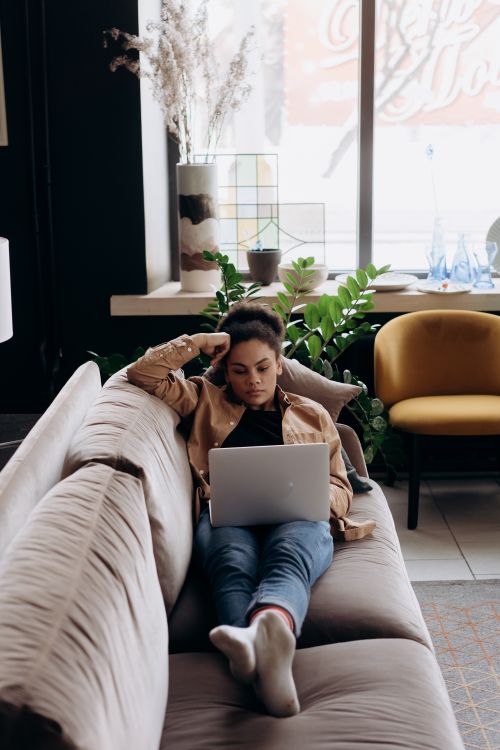 Free A woman working remotely on a laptop at home, lying on a comfortable sofa. Stock Photo