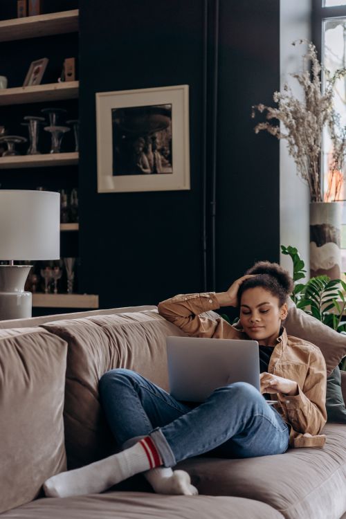 Free African American woman relaxing with laptop on a comfy couch at home. Stock Photo