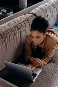 Young woman lying on a sofa working on a laptop, representing remote work and home office lifestyle.
