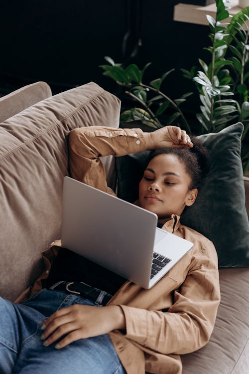 Free A Woman Resting on a Couch while Looking at the Screen of her Laptop Stock Photo