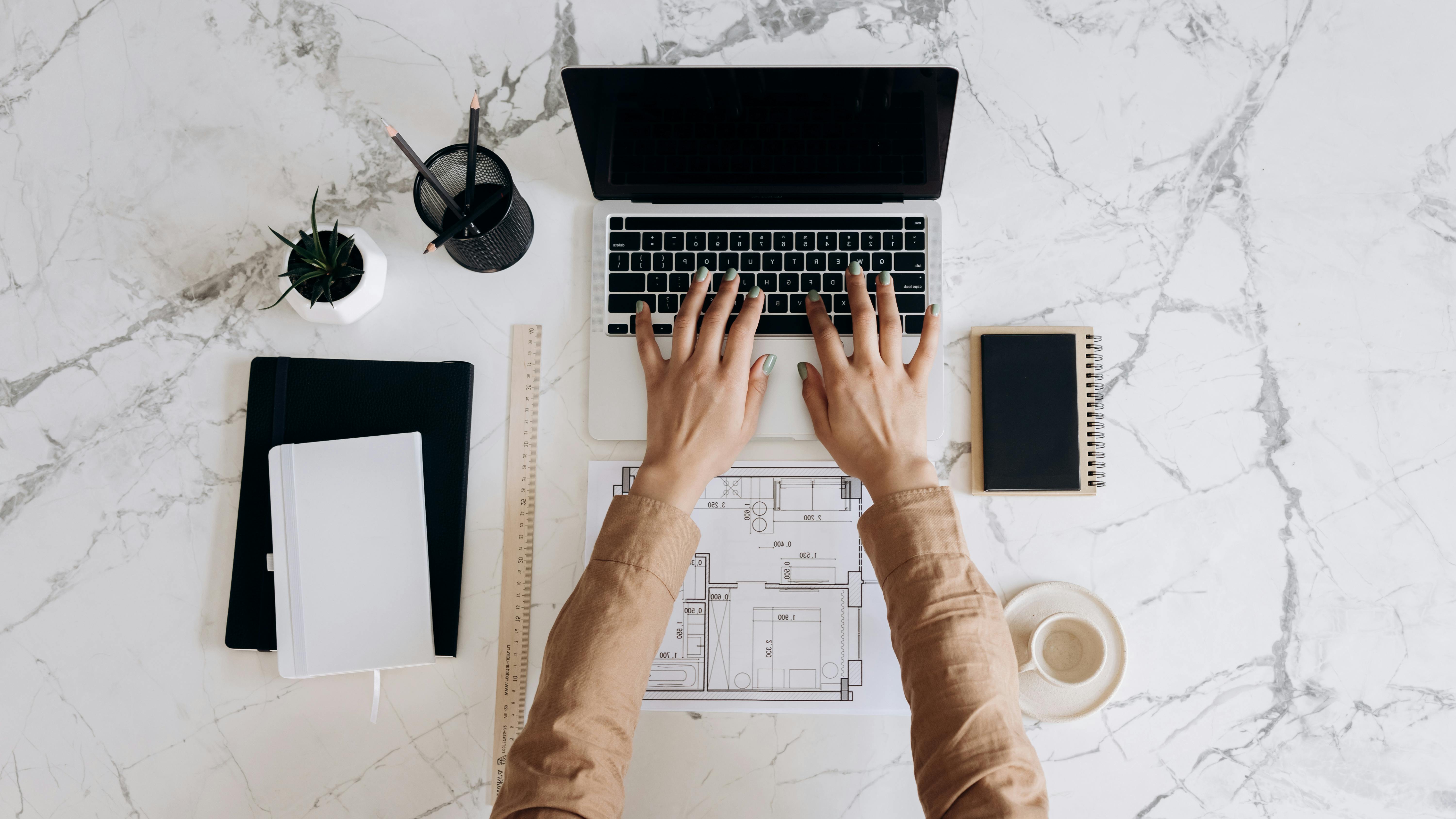 Top view of a workspace with a laptop, coffee, and office supplies on a marble table.