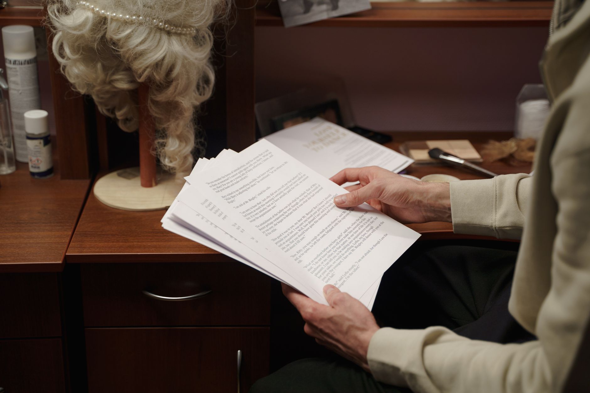 An actor reviews a script in a backstage dressing room, preparing for a theater rehearsal.