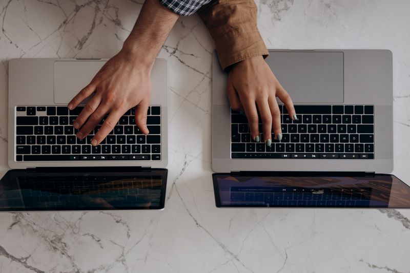 Two individuals typing on laptops from a top view angle, showcasing collaborative work.