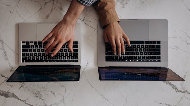 Two individuals typing on laptops from a top view angle, showcasing collaborative work.