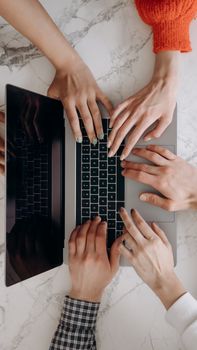 A top-down view of multiple hands typing on a laptop keyboard on a marble desk, indicating teamwork.