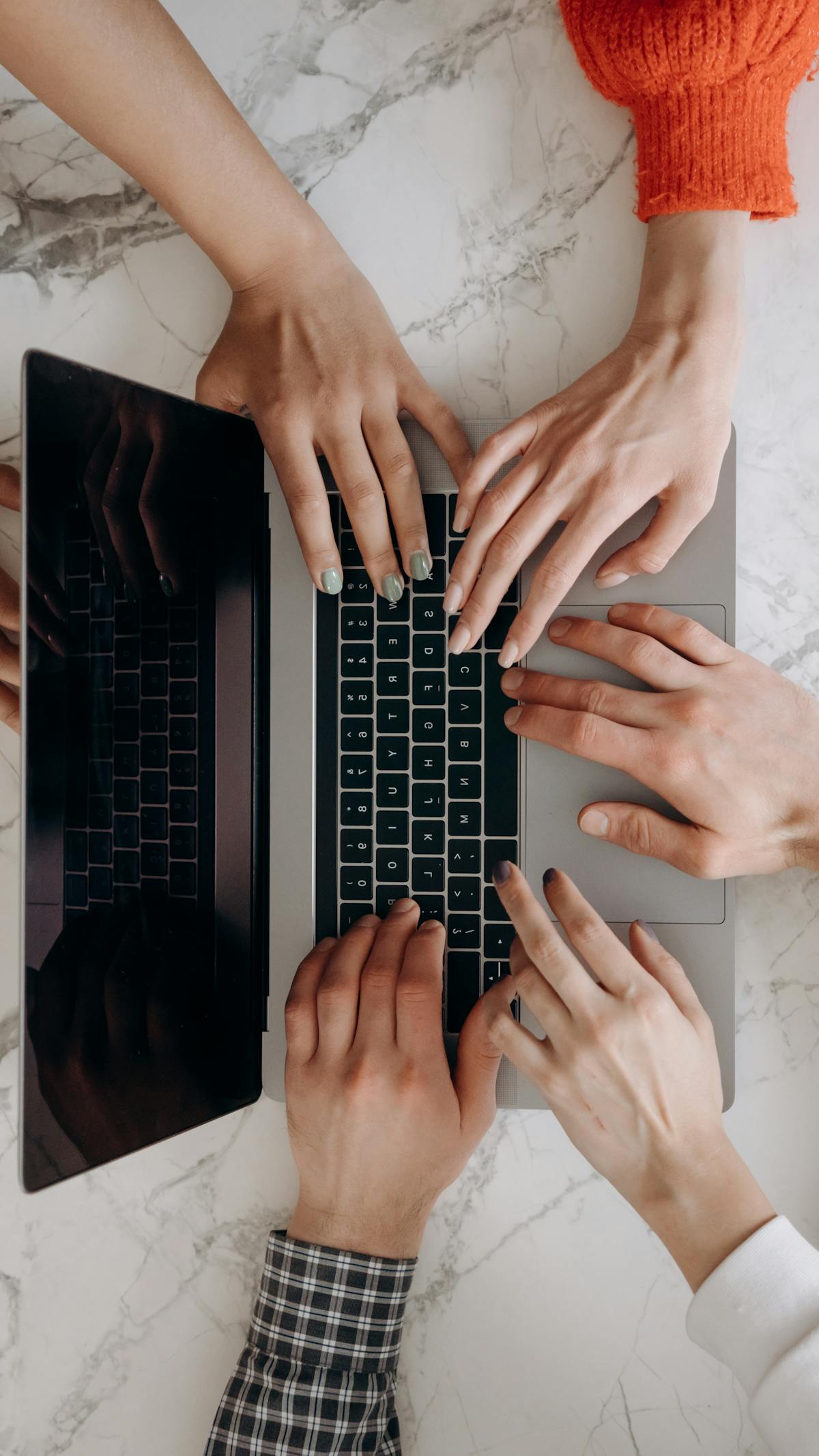 Mani di più persone che digitano su tastiera di un laptop