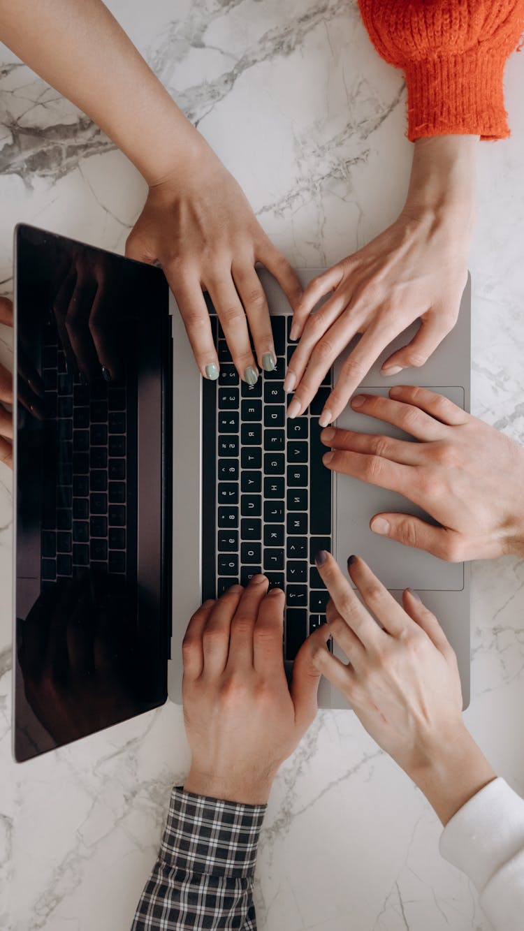 Overhead Shot Of People's Hands Typing On A Laptop Keyboard