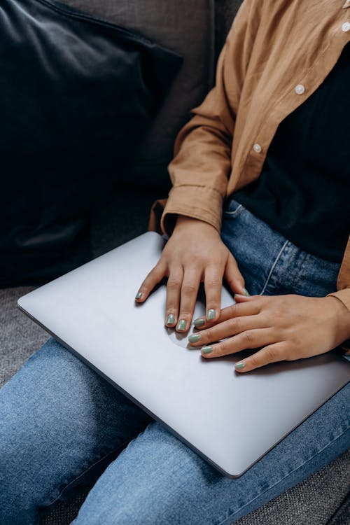 Vrouw In Bruin Shirt Met Lange Mouwen En Blauwe Spijkerbroek Zittend Op De Bank Met Laptop