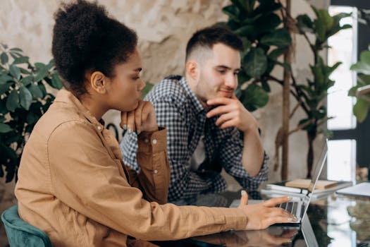 Two colleagues working together on a laptop in a stylish indoor office with plants.