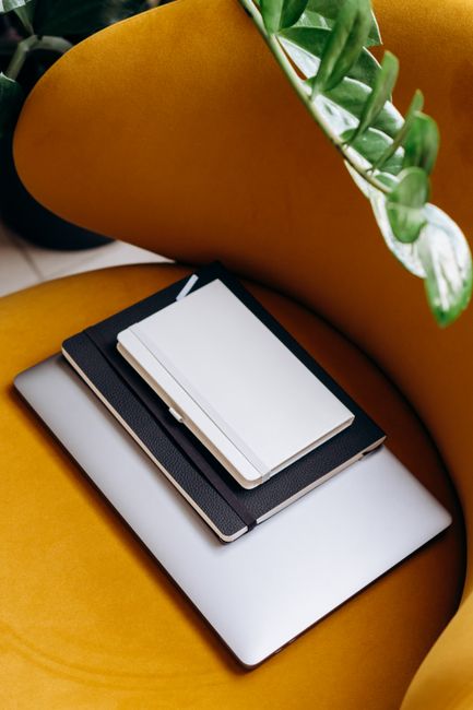 Fotomural Espacio de trabajo elegante con cuadernos y un portátil en un sillón mostaza decorado con hojas verdes.
