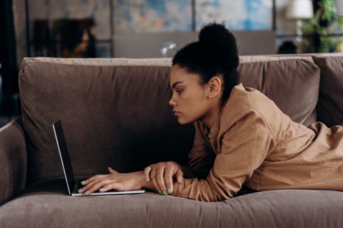 Free African American woman lying on sofa working remotely on her laptop. Stock Photo
