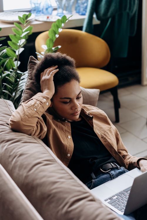 Free A relaxed woman using a laptop while leaning back on a sofa in a cozy home environment. Stock Photo