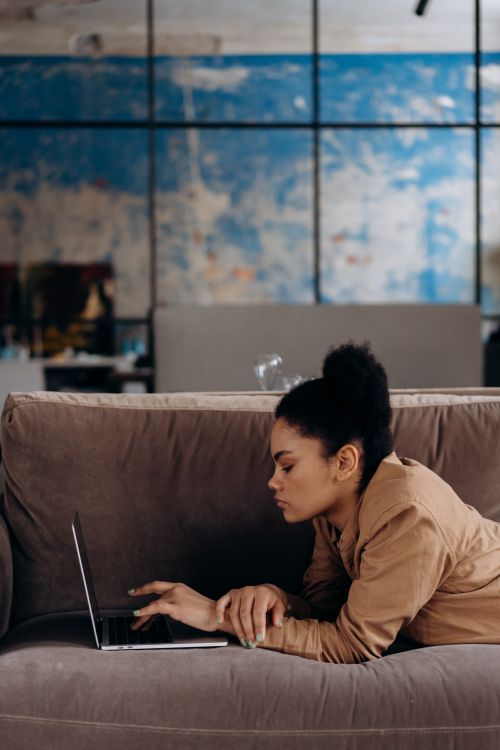 Free Young woman lying on a sofa browsing her laptop indoors. Casual and relaxed atmosphere. Stock Photo
