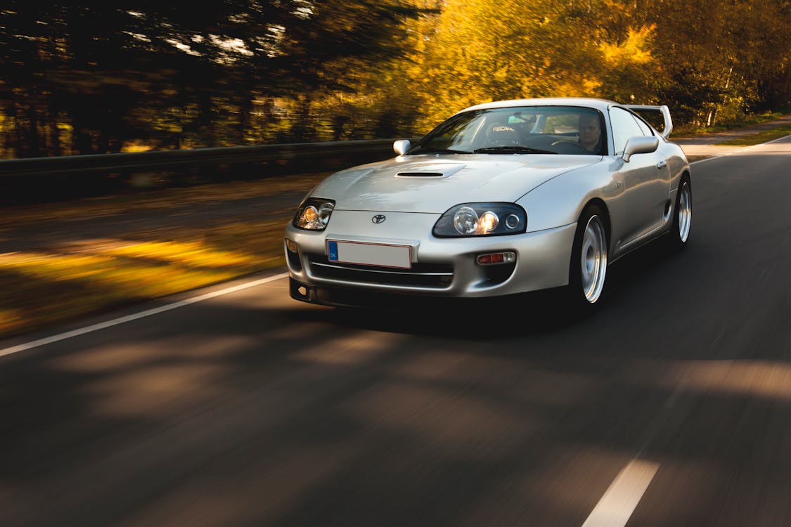 Free Man Driving A Silver Toyota Supra on Road Stock Photo