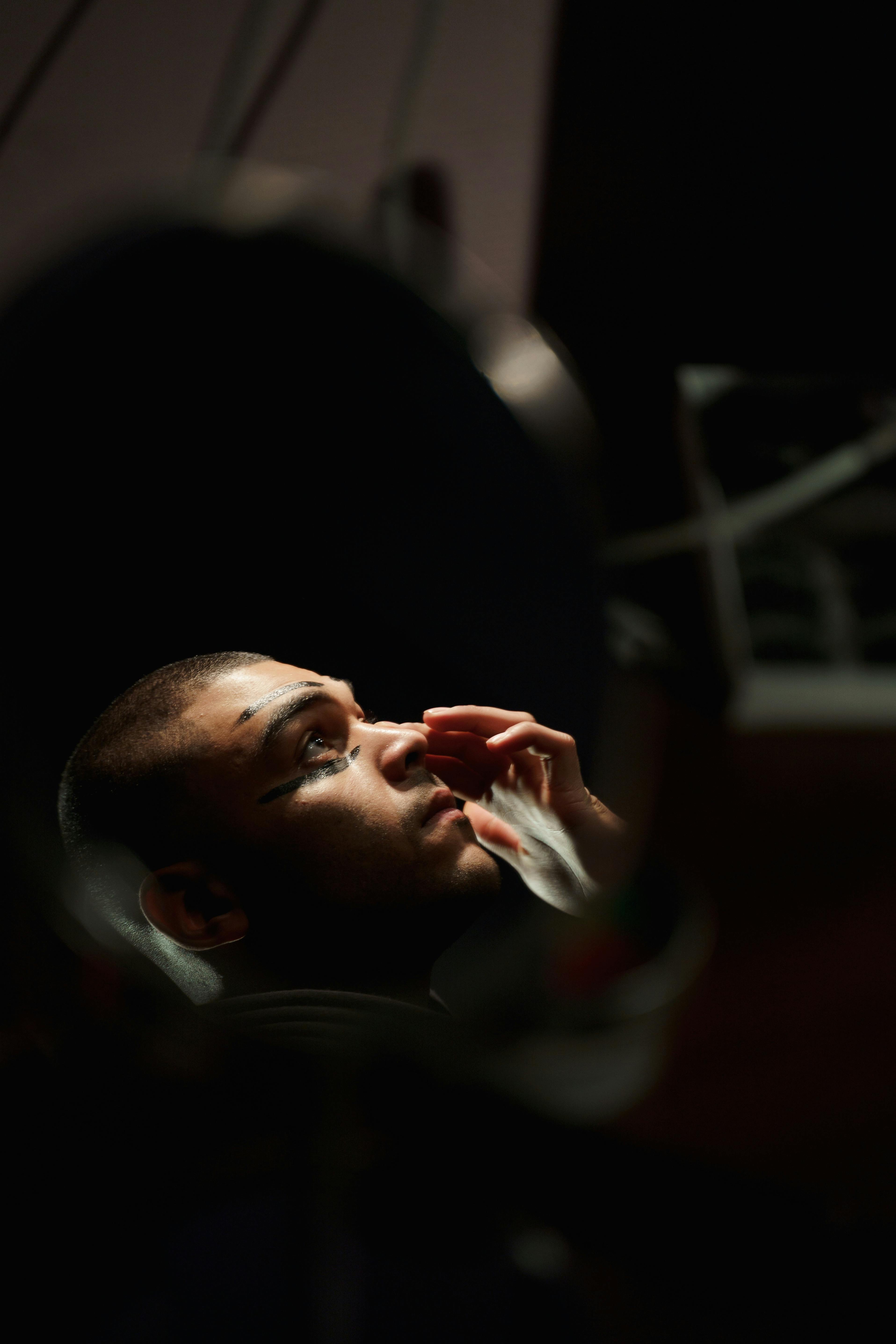 Free An actor applies makeup in a dark theater setting, seen reflected in a mirror. Stock Photo