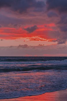 Vibrant ocean sunset with dramatic red clouds and gentle waves creating a captivating seascape.