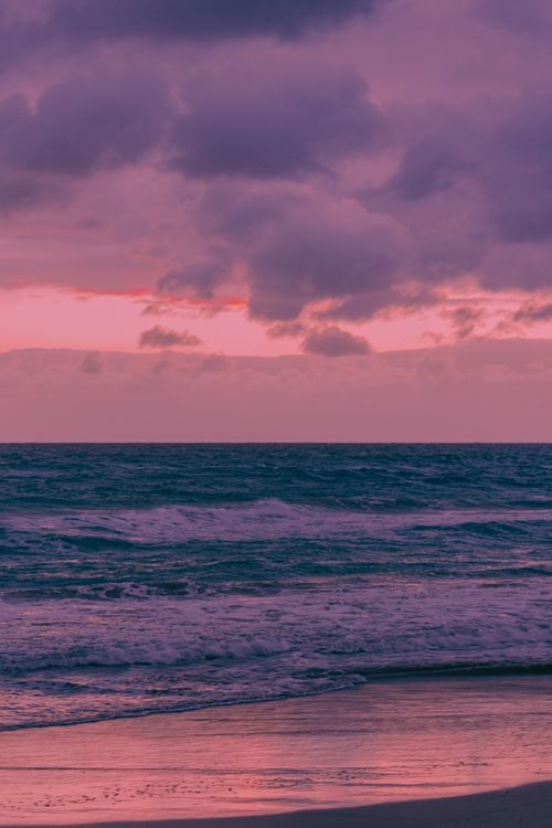 Free A serene beach scene with a dramatic cloudy sky and twilight hues over the ocean. Stock Photo