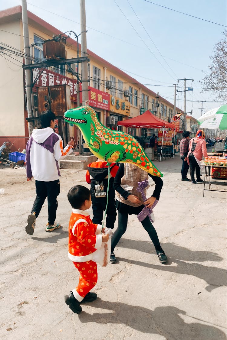 Little Boy Walking In City With A Dinosaur Balloon 