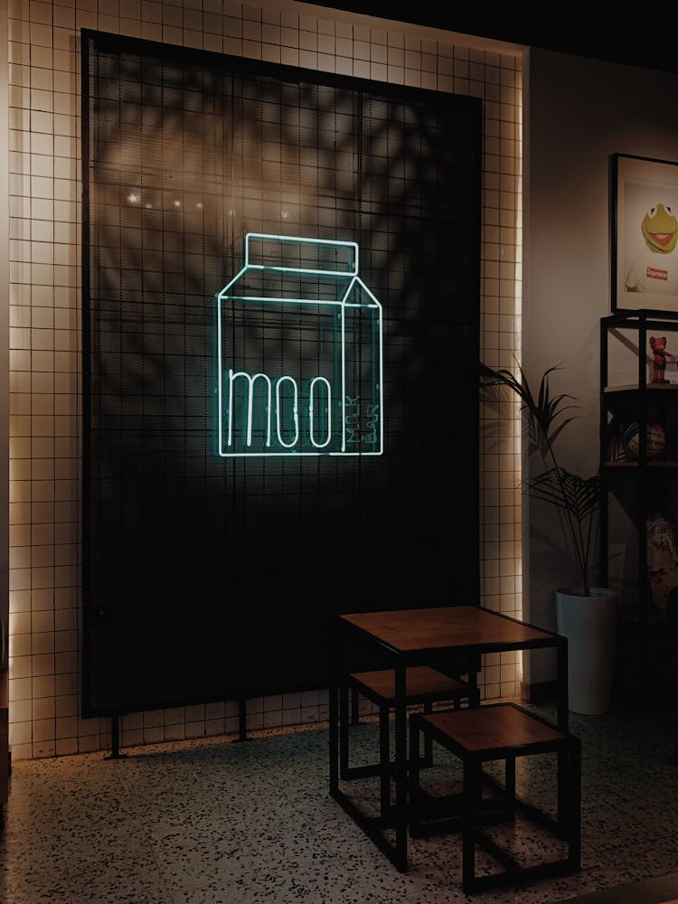 Neon Signboard With Milk Box And Word Moo Near Table