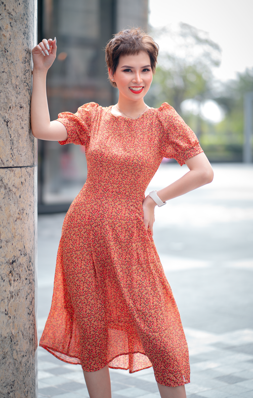 Free Stylish young woman smiling in red floral dress enjoying a bright summer day outdoors. Stock Photo