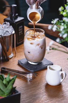 Close-up of cream being poured into iced coffee on a wooden table.