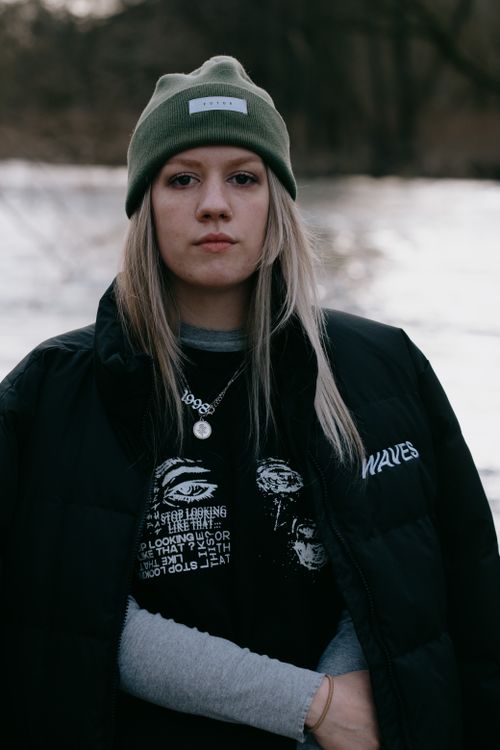 Free Portrait of a woman wearing winter clothing by a riverside, showcasing casual style. Stock Photo