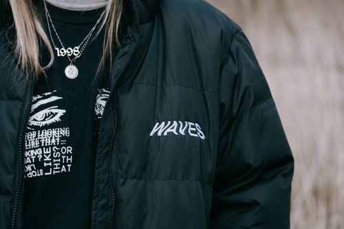 Free Close-up of a person wearing a black puffer coat and layered necklaces outdoors. Stock Photo