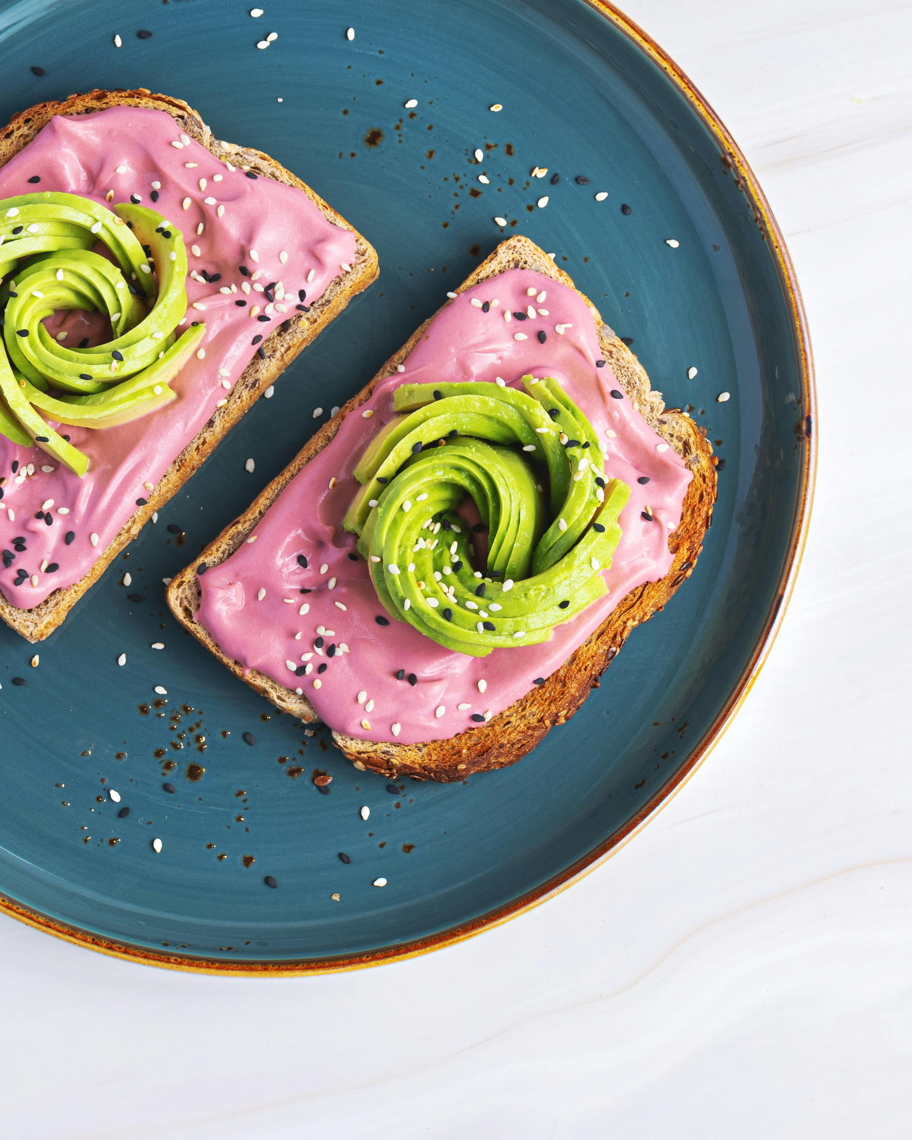 Artistic depiction of avocado toast on a ceramic plate with a vibrant pink spread, ideal for food photography.