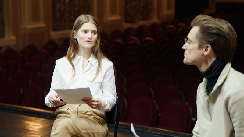 A man and woman rehearsing a play script on a theater stage during the day.