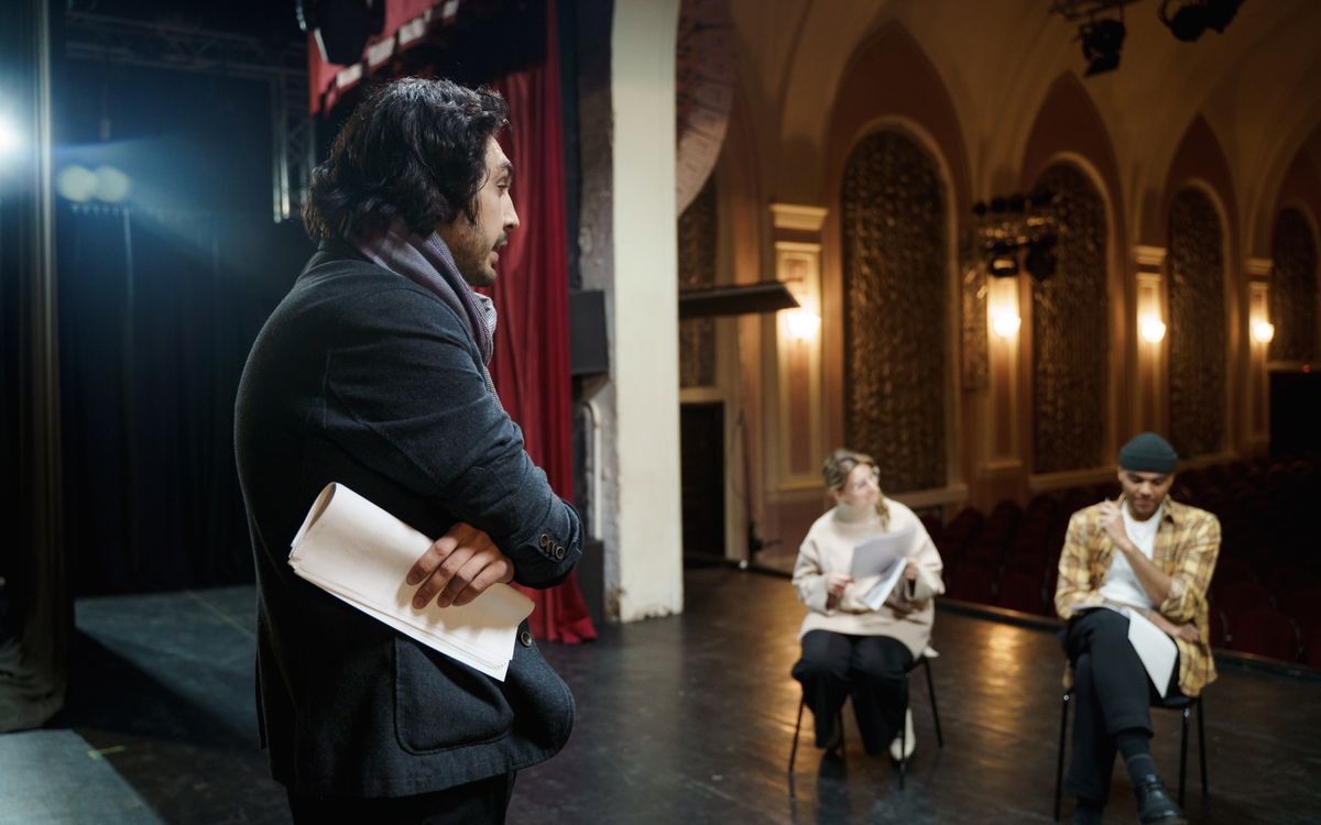 Actors rehearsing on stage in a vintage theater auditorium with a director observing.