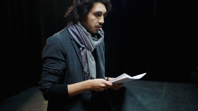 Male actor rehearsing lines on stage in a dimly lit theater environment.