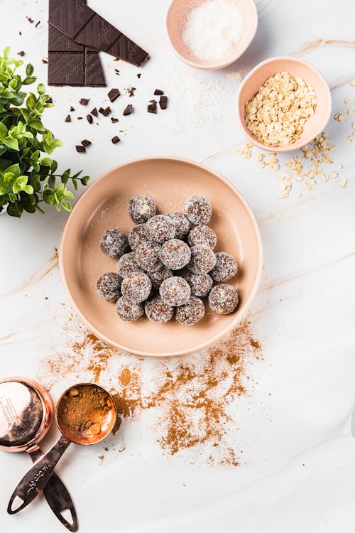 Free Top view of delicious chocolate candies with coconut flakes in bowl near spoons with cacao powder and plant next to bowl with sugar and oatmeal on table Stock Photo