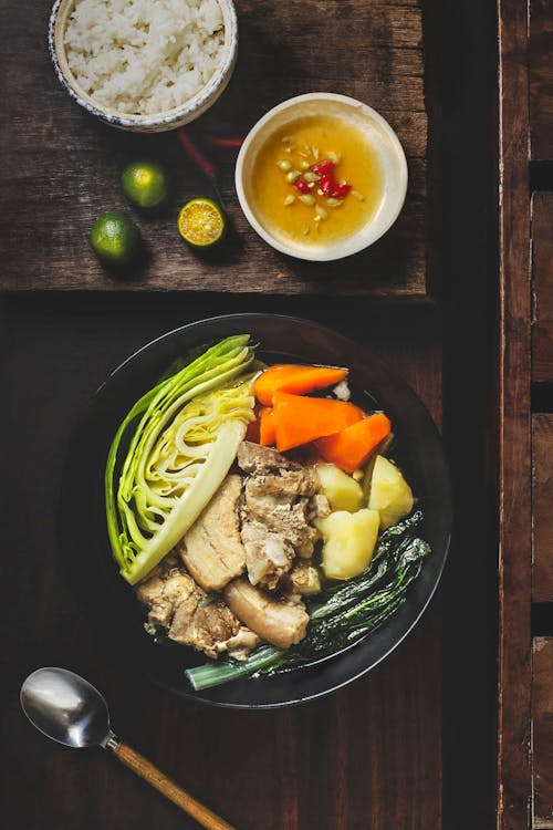 Free Top view of bowl with potatoes and carrot with cabbage and meat placed on table near spoon and rice and sauce Stock Photo